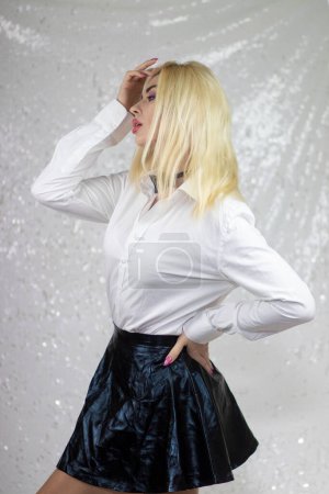 Téléchargez les photos : Mannequin femme blonde en chemise blanche et jupe noire avec noeud papillon, dans le style de surréalisme pop gothique, fond gris clair et blanc, xmaspunk, argent et noir, froissé - en image libre de droit