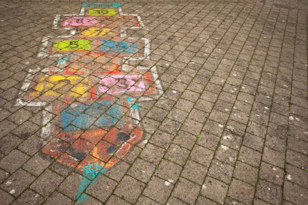 Téléchargez les photos : Hopscotch game drawn with coloured chalks on stone-block paved road. Copy-space. Outdoor shot - en image libre de droit