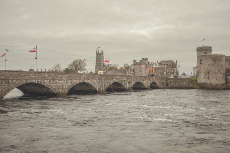 Foto de Discover Ireland concept. View to Thomond Bridge over Shannon River and King John's Castle in Limerick city. Cloudy weather. Text space. Postcard style. Outdoor shot - Imagen libre de derechos