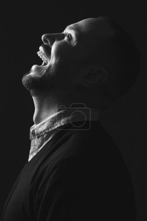 Photo for Demonic laughter concept. Portrait of charismatic 40-year-old man posing over black background and laughing. Short haircut. Classic, smart casual style. Black and white studio shot - Royalty Free Image