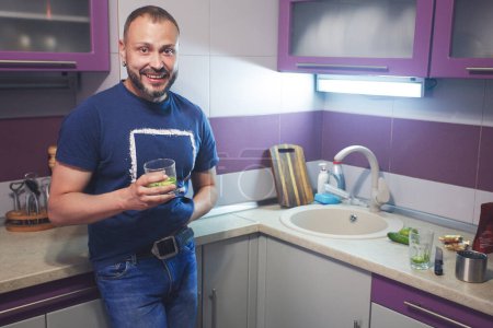 Photo for Housewarming Party concept. Happy smiling mature bearded man standing with a drink in his new modern kitchen. Indoor shot - Royalty Free Image
