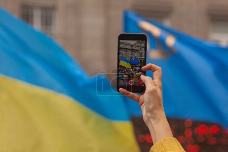 Photo for Ukrainians and supporters rally. The first anniversary of Russia's invasion of Ukraine. Hand shooting meeting on mobile phone. Close up. Copy space. Outdoor shot - Royalty Free Image