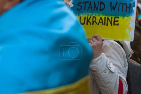 Photo for Ukrainians and supporters rally concept. The first anniversary of Russia's invasion of Ukraine. Woman holding banner Stand with Ukraine. Outdoor shot - Royalty Free Image