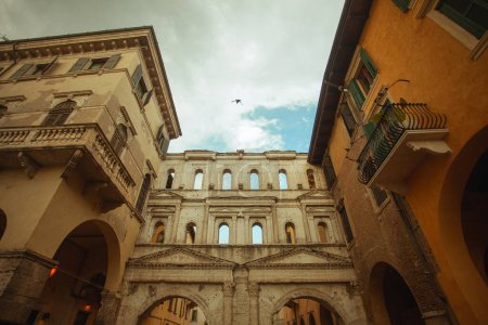 Foto de Concepto Verona justo. Lado frontal de Porta Borsari en el casco antiguo de la ciudad. Clima nublado. Pájaro volador en el cielo. Toma al aire libre con perspectiva - Imagen libre de derechos