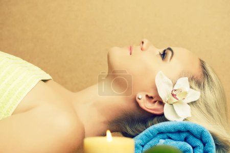 Photo for Relaxation procedures concept. Portrait of a beautiful young woman at spa salon. Perfect skin and long blond hair with white orchid. Text space. Close up. Indoor shot - Royalty Free Image