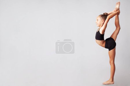Photo for Acrobatic choreography concept. Full length profile portrait of smiling young little gymnast showing her skills isolated on gray background. Copy-space. Studio shot - Royalty Free Image