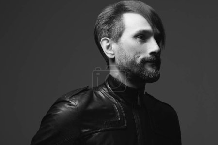 Photo for Rock star concept. Profile portrait of fashionable handsome mature biker in leather jacket over dark gray background. Close up. Copy-space. Retro style. Black and white studio shot - Royalty Free Image