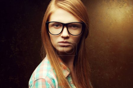 Photo for Geek Girlfriend concept. Portrait of young beautiful red-haired woman wearing trendy glasses and casual shirt, posing over golden background. Hipster style. Close up. Text space. Studio shot - Royalty Free Image