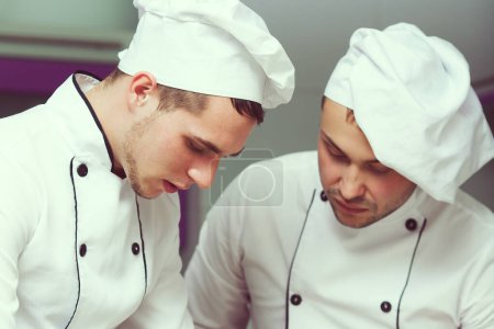Photo for Cooking process concept. Portrait of two working men in cook uniform making food. Close up. Indoor shot - Royalty Free Image