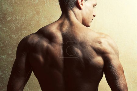 Foto de Belleza masculina y concepto deportivo. Retrato de modelo masculino musculoso guapo con una espalda increíble posando sobre fondo dorado. Cuerpo de atleta perfecto. De cerca. Captura de estudio - Imagen libre de derechos