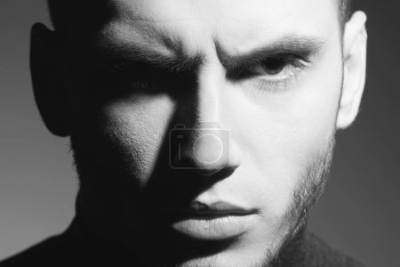 Photo for Revenge concept. Close up portrait of handsome brutal young manl with stubble posing over gray background. Classic style. Black and white studio shot - Royalty Free Image