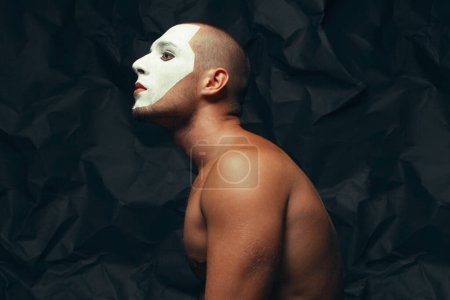 Photo for Behind curtains concept. Arty portrait of circus performer over black wrinkled background. White mask on face. Muscular body and perfect tan. Close up. Text space. Studio shot - Royalty Free Image