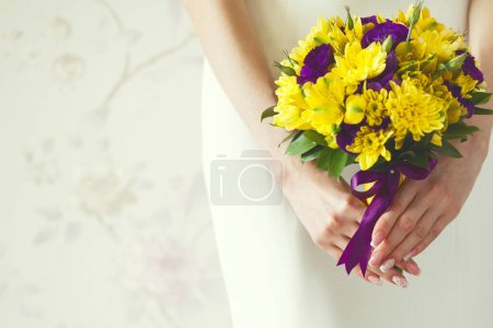 Téléchargez les photos : Mains de mariée avec bouquet de mariage en fleurs violettes et jaunes sur robe blanche élégante. Fond vintage. Style rétro. Ferme là. Espace de copie. Plan intérieur - en image libre de droit