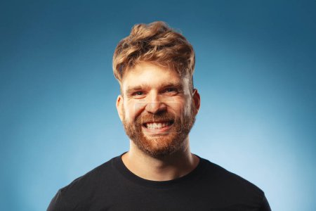 Photo for Male beauty concept. Emotive portrait of laughing charismatic active 30-year-old man posing over blue background. Perfect haircut. Whity shiny smile. Text space. Close up. Studio shot - Royalty Free Image