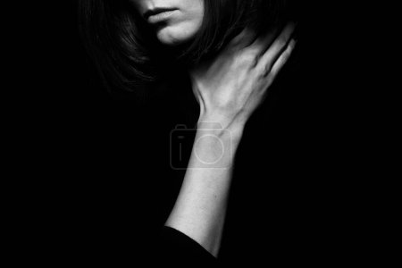 Foto de Concepto de violencia doméstica. Retrato de cerca de una joven mujer escondiendo la cara posando con la mano en el cuello aislada sobre fondo negro. Emoción humana, expresión, derechos, comunicación. Espacio de texto. Monocromo tiro - Imagen libre de derechos