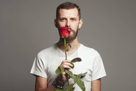 Photo for Male beauty concept. Portrait of romantic charismatic 30-year-old man posing over gray background. with red rose Perfect haircut. Hipster style. Text space. Studio shot - Royalty Free Image