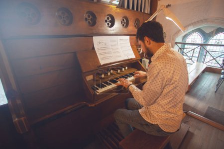Photo for Portrait of young handsome man playing the old organ in Irish church. Perspective. Indoor shot - Royalty Free Image