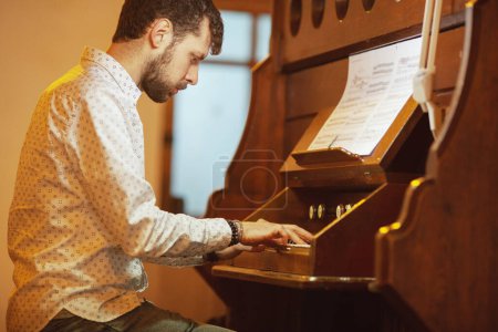 Téléchargez les photos : Jeune homme beau jouant du vieil orgue dans une église irlandaise. Plan intérieur - en image libre de droit