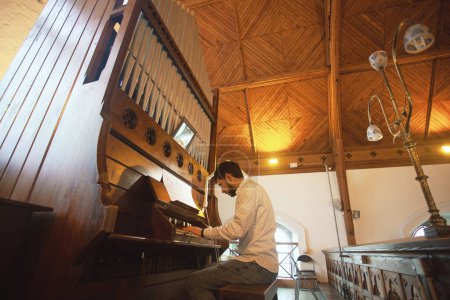 Téléchargez les photos : Portrait d'un jeune homme beau jouant du vieil orgue dans une église irlandaise. Perspective. Plan intérieur - en image libre de droit