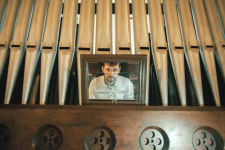 Photo for Artistic portrait of young handsome man playing the old organ in Irish church. Indoor shot - Royalty Free Image