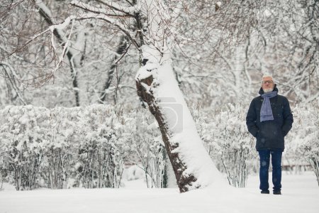 Photo for Full length portrait of handome mature man in trendy winter clothing and fashionable glasses standing in snow park. Text space. Outdoor shot - Royalty Free Image
