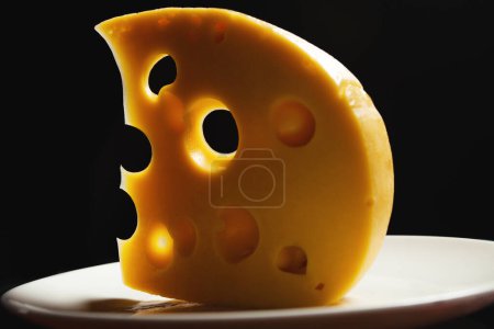 Photo for Milk product concept. Piece of european cheese in form of crescent moon lying on white plate over black background symbolizing outter space. Surreal, abstract style. Close up. Studio shot - Royalty Free Image