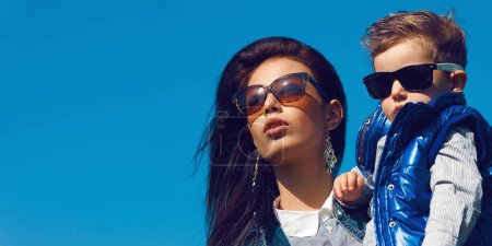 Photo for Portrait of fashionable baby boy and his gorgeous mother (hollywood star) in trendy sunglasses walking in the street. Sunny spring day. Close up. Copy-space. Outdoor shot - Royalty Free Image