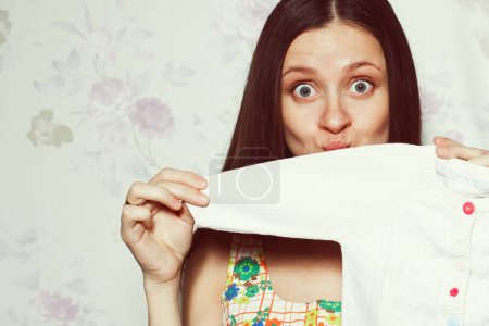 Photo for Stylish pregnancy concept: portrait of funny young woman in summer dress holding small size baby shirt. Vintage, retro style. Copy-space. Close up. Studio shot - Royalty Free Image