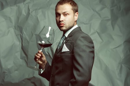 Photo for Sommelier concept. Emotive portrait of handsome stylish man in elegant classic dark gray suit drinking red wine. Baroque retro style. Studio shot - Royalty Free Image