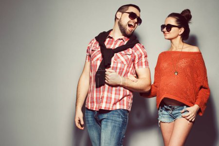 Photo for Stylish pregnancy & family concept: portrait of funny couple of hipsters (husband and wife) in trendy casual clothing, eyewear smiling and posing over gray background. Urban street style. Copy-space. Studio shot - Royalty Free Image