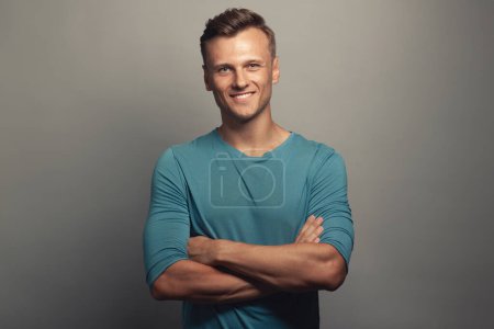 Photo for Male beauty concept. Portrait of smiling 30-year-old man standing over gray background with crossed hands. Classic style. Wavy glossy blond hair. Copy-space. Studio shot - Royalty Free Image