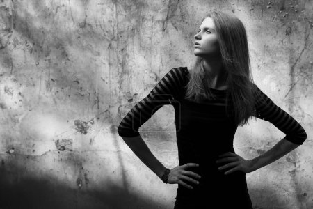 Photo for Arty portrait of beautiful model in black striped cocktail dress posing over old stone wall with metal constructions. Film noir style. Text space. Black and white (monochrome) outdoor shot - Royalty Free Image