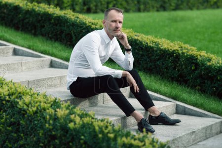 Photo for Luxurious, stylish concept. Rich mature man sitting on marble stairs. Premium class clothing, leather footwear, expensive wrist watch, excellent manicure. Classic style. Text space. Outdoor shot - Royalty Free Image