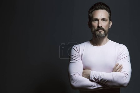 Photo for Fabulous at any age, male beauty concept. Portrait of 45-year-old man standing over dark gray background. Classic style. Scar on forehead. Hands crossed. Copy-space. Studio shot - Royalty Free Image