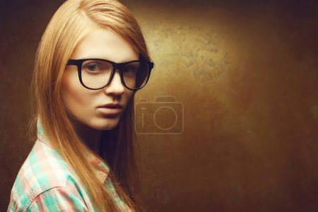 Photo for Portrait of a young beautiful red-haired wearing trendy glasses and casual shirt and posing over golden background. Close up. Copy-space. Studio shot - Royalty Free Image