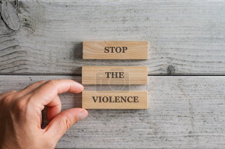 Photo for Male hand stacking three wooden pegs with a Stop the violence sign on them. Over simple white background. - Royalty Free Image