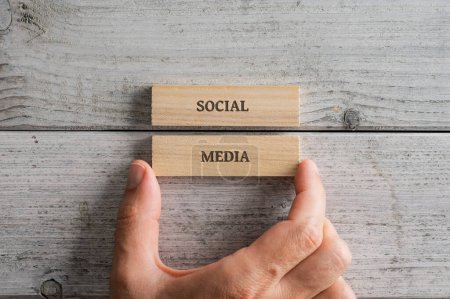 Téléchargez les photos : Male hand stacking two wooden pegs with a Social media sign on them. Over textured white wooden background. - en image libre de droit