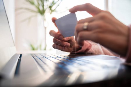 Foto de Closeup view of female hands holding a credit card over a laptop computer in a conceptual image of online shopping. - Imagen libre de derechos