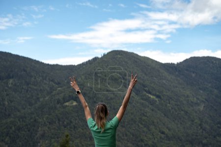Foto de Vista desde atrás de una mujer con las manos victoriosas levantadas en alto en el aire de pie afuera mirando las montañas. Un hermoso viaje de vida. - Imagen libre de derechos