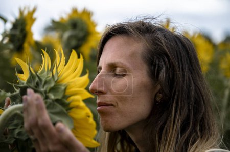 Foto de Vista de cerca de una joven sosteniendo suavemente un hermoso girasol en flor que crece en el campo oliendo y disfrutando de su esencia. - Imagen libre de derechos