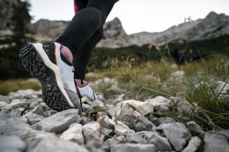 Foto de Vista de ángulo bajo ligeramente desde el lado de una hembra zapatos de senderismo como ella camina sobre piedras y rocas hasta una alta montaña. - Imagen libre de derechos