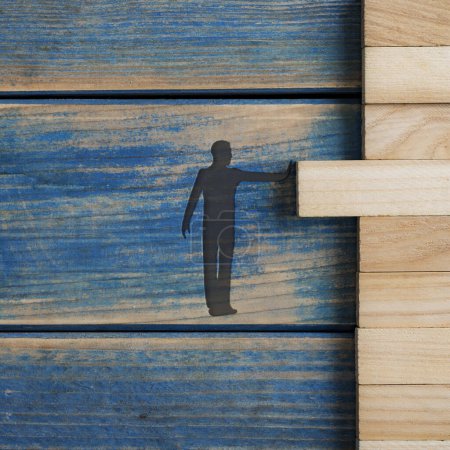 Foto de Silueta de un hombre empujando una clavija de madera en blanco en un stac de ellos en una imagen conceptual de la creación de empresas, visión e idea. Sobre fondo azul texturizado. - Imagen libre de derechos