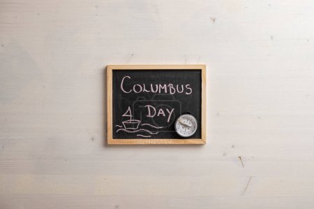 Foto de Vista superior de una pequeña pizarra con un letrero del día de Colón escrito en ella y una brújula. Sobre fondo de madera trenzado simple con espacio de copia. - Imagen libre de derechos