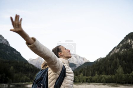 Foto de Vista del perfil de una mujer joven, una excursionista, de pie en medio de una hermosa naturaleza de montaña con los brazos extendidos, disfrutando de su vida. - Imagen libre de derechos