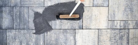 Foto de Vista superior de una escoba cepillando huecos de baldosas de arena entre baldosas de cemento en un patio o acera recién pavimentada. - Imagen libre de derechos