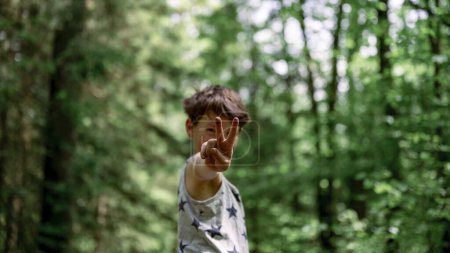 Foto de Joven adolescente mostrando un gesto de victoria directamente hacia la cámara de pie fuera en la hermosa naturaleza verde. - Imagen libre de derechos