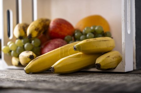 Foto de Fruta fresca mixta - naranjas, manzanas, plátanos y uvas - en una caja de madera sobre tableros de madera rústicos texturizados. - Imagen libre de derechos