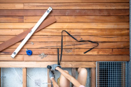 Foto de Vista aérea de una mujer en un proyecto de bricolaje doméstico: atornillar un tornillo en una plancha de madera para un nuevo patio al aire libre. Con herramientas a su lado. - Imagen libre de derechos
