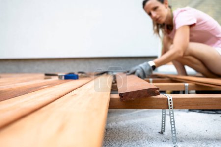 Foto de Vista de ángulo bajo de una mujer en un proyecto de bricolaje en casa colocando tablón de madera en un marco de cimentación para un nuevo patio de madera. - Imagen libre de derechos