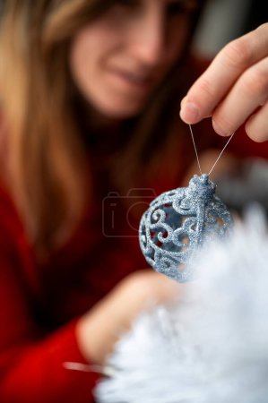 Foto de Mujer joven decorando un árbol de Navidad blanco con brillante bola de vacaciones azul. - Imagen libre de derechos